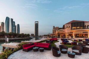 جلسات ومقاعد مريحة لمطعم شاطئي يطل على المارينا وأفق أبراج خارجية كورنيش أبوظبي في نهار مشمس.