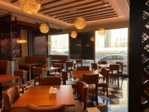 تصميم داخلي لمطعم في النهدة يضم طاولات وكراسي خشبية مع إضاءة لطيفة ونوافذ الشوارع على النوافذ.