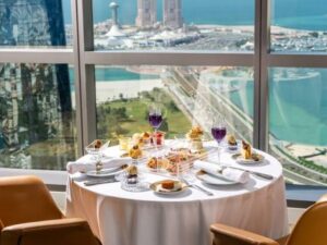 تصميم داخلي فسيح ومشرق لمطعم يطل على البحر يضم مقاعد خضراء مريحة وطاولات خشبية مع منضدة بوفيه طويلة على الجانب.